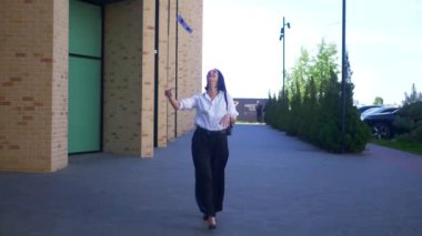 İş kadını, iş merkezinin yakınına menkul kıymetler bırakıyor. Yavaş çekim. Ofis çalışanı, tatil, yönetmen, resmi kıyafetler. Beyaz tişörtlü ve siyah pantolonlu mutlu bayan bitirdikten sonra değerli belgeleri sokağa saçıyor.