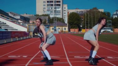 Stadyum pistinde neşeyle dans eden iki ateşli kadın. Yavaş çekim. Kısa etekli ponpon kızlar koşu pistinde mutlu bir şekilde dans ediyorlar. İki kız spor pistinde baştan çıkarıcı bir şekilde dans ediyor. Kadınlar enerjik bir şekilde dans ediyor 