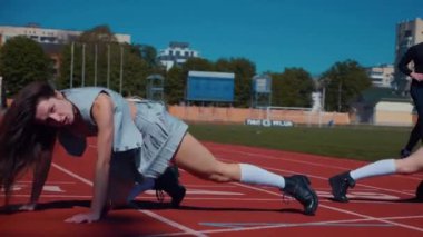 Stadyum pistinde neşeyle dans eden iki ateşli kadın. Yavaş çekim. Kısa etekli ponpon kızlar koşu pistinde mutlu bir şekilde dans ediyorlar. İki kız spor pistinde baştan çıkarıcı bir şekilde dans ediyor. Kadınlar enerjik bir şekilde dans ediyor 