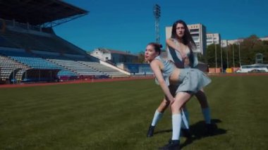 Stadyum pistinde neşeyle dans eden iki ateşli kadın. Yavaş çekim. Kısa etekli ponpon kızlar koşu pistinde mutlu bir şekilde dans ediyorlar. İki kız spor pistinde baştan çıkarıcı bir şekilde dans ediyor. Kadınlar enerjik bir şekilde dans ediyor 