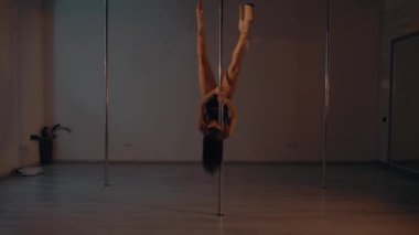 Woman in leather underwear gracefully pole dancing in a dimly lit room. Elegant female in a bikini performer doing a seductive dance on a pole. Lady showing her strength and flexibility on pole. Sensual dance performance by a woman on a metal pole