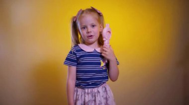 Küçük kız sıcakta bir vantilatörle kendine üflüyor. Genç kız seve seve sarı arka planda yelpaze tutar. Çocuk parlak sarı arka planda bir çocuk yelpazesi tutuyor.