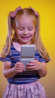Dikey olarak, küçük bir kız hevesle çocuk elektronik oyunu oynuyor. Mutlu bir çocuk sarı arka planda çocuk yapbozu oynuyor. Küçük bir çocuk gülüyor ve mutlu bir oyun oynuyor..