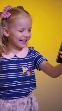 Çocuk telefondaki video konuşmasında eğleniyor gibi. Dikey. Elinde akıllı telefon kamerasıyla gülümseyen kız. Genç bir kız arıyor ve telefonuyla fotoğraf çekiyor. Küçük kız telefonunu kullanıyor..