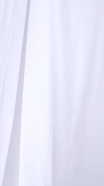 Beyaz şeffaf kumaş rüzgarda dalgalanıyor. Dikey. Parlak bir stüdyoda uzun beyaz perdeler. Rüzgarda savrulan saf beyaz perdeler. Ağır çekim. Görüntüler. Güneşli bir odada beyaz bir perde yükseliyor. Yumuşak, dalgalı beyaz perde huzur içinde 