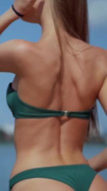 Sahilde bikinili genç bir kadın. Dikey. Esnek kalçalı bir kız kumsalda güneşleniyor. Çekici, ince model kameraya poz veriyor. Bikinili bir kadın kumsalda dinleniyor. Bikinili güzellik plaj havasından zevk alıyor..