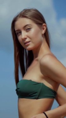 Sahilde bikinili genç bir kadın. Dikey. Esnek kalçalı bir kız kumsalda güneşleniyor. Çekici, ince model kameraya poz veriyor. Bikinili bir kadın kumsalda dinleniyor. Bikinili güzellik plaj havasından zevk alıyor..