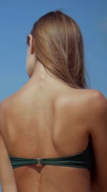 Sahilde bikinili genç bir kadın. Dikey. Esnek kalçalı bir kız kumsalda güneşleniyor. Çekici, ince model kameraya poz veriyor. Bikinili bir kadın kumsalda dinleniyor. Bikinili güzellik plaj havasından zevk alıyor..