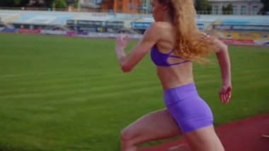 Stadyumda koşan genç bir kadın. Pistte koşan bayan sporcu. Koşu pistinde koşan güzel bir bayan atlet. Şortlu kararlı bir kadın ve güneşli havalarda her şey yolunda. Kadın model koşucu iş başında. Başlar
