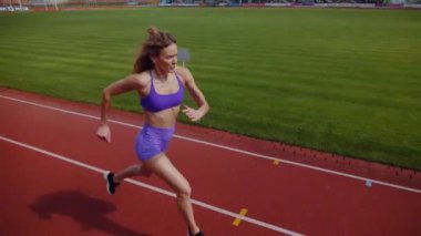 Stadyumda koşan genç bir kadın. Pistte koşan bayan sporcu. Koşu pistinde koşan güzel bir bayan atlet. Şortlu kararlı bir kadın ve güneşli havalarda her şey yolunda. Kadın model koşucu iş başında. Başlar
