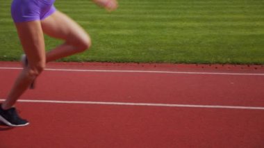 Stadyumda koşan genç bir kadın. Pistte koşan bayan sporcu. Koşu pistinde koşan güzel bir bayan atlet. Şortlu kararlı bir kadın ve güneşli havalarda her şey yolunda. Kadın model koşucu iş başında. Başlar