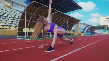 Genç bir kadın antrenmana hazırlanıyor. Spor meraklısı koşu parkurunda topallıyor. Hareketli kadın egzersiz öncesi esneme hareketleri yapıyor. Koşucu sporcu esneme hareketleriyle ısınıyor. Dişi koşucu ön koşular yapıyor