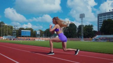 Genç bir kadın antrenmana hazırlanıyor. Spor meraklısı koşu parkurunda topallıyor. Hareketli kadın egzersiz öncesi esneme hareketleri yapıyor. Koşucu sporcu esneme hareketleriyle ısınıyor. Dişi koşucu ön koşular yapıyor