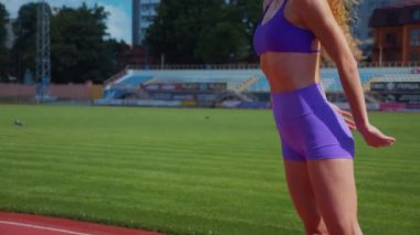 Genç bir kadın antrenmana hazırlanıyor. Spor meraklısı koşu parkurunda topallıyor. Hareketli kadın egzersiz öncesi esneme hareketleri yapıyor. Koşucu sporcu esneme hareketleriyle ısınıyor. Dişi koşucu ön koşular yapıyor