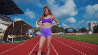 Genç bir kadın antrenmana hazırlanıyor. Spor meraklısı koşu parkurunda topallıyor. Hareketli kadın egzersiz öncesi esneme hareketleri yapıyor. Koşucu sporcu esneme hareketleriyle ısınıyor. Dişi koşucu ön koşular yapıyor