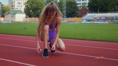 Genç bir kadın antrenmana hazırlanıyor. Spor meraklısı koşu parkurunda topallıyor. Hareketli kadın egzersiz öncesi esneme hareketleri yapıyor. Koşucu sporcu esneme hareketleriyle ısınıyor. Dişi koşucu ön koşular yapıyor