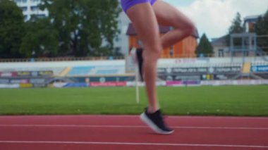 Genç bir kadın antrenmana hazırlanıyor. Spor meraklısı koşu parkurunda topallıyor. Hareketli kadın egzersiz öncesi esneme hareketleri yapıyor. Koşucu sporcu esneme hareketleriyle ısınıyor. Dişi koşucu ön koşular yapıyor