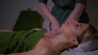 Güzel çıplak kız boynuna ve göğsüne masaj yaptırıyor. Tanımlanamayan genç bir kadın spa salonunda profesyonel sırt masajı yaptırıyor. Yakın plan çekim. Lüks profesyonel masaj anlayışı. Ağır çekimde çekmek.