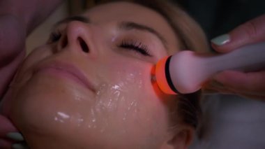 Genç bir kadın spa salonunda profesyonel donanım titreşim yüz masajı yaptırıyor. Güzel kız yüzüne rahatlatıcı bir masaj yaptırıyor. Yakın plan çekim. Lüks profesyonel masaj anlayışı. Ağır çekimde çekmek.