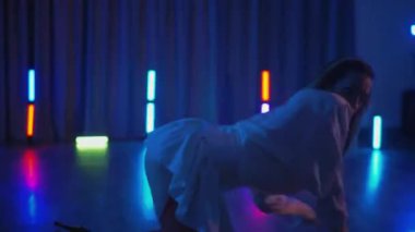 Beyaz şeffaf elbiseli, erotik dans eden ve yüksek topuklu ayakkabı giyen genç bir kadın. Siyah şortlu yarı traşlı kız karanlık uzayda zarafetle hareket ediyor. Sahnedeki bir disko kulübünde striptiz. Kadın dansçı, siluet karşısında 