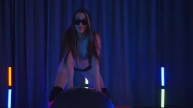 Anime tarzında siyah gözlüklü genç bir kadın erotik bir şekilde dans ediyor. Siyah şortlu yarı traşlı kız karanlık uzayda zarafetle hareket ediyor. Sahnedeki bir disko kulübünde striptiz. Gölgeli bir arka planda silueti olan kadın dansçıya tezahürat