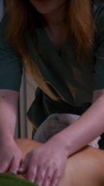 Dikey, güzel çıplak kız sırtına, bacaklarına ve ellerine masaj yaptırıyor. Tanımlanamayan genç bir kadın spa salonunda profesyonel sırt masajı yaptırıyor. Yakın plan çekim. Lüks profesyonel masaj anlayışı. Ağır çekimde çekmek.