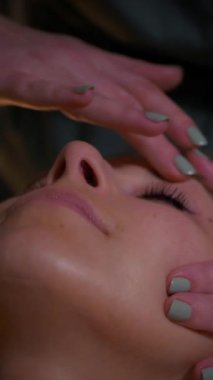 Dikey, güzel çıplak kız yüzüne rahatlatıcı bir masaj yapıyor. Tanımlanamayan genç bir kadın spa salonunda profesyonel sırt masajı yaptırıyor. Yakın plan çekim. Lüks profesyonel masaj anlayışı. Ağır çekimde çekmek.