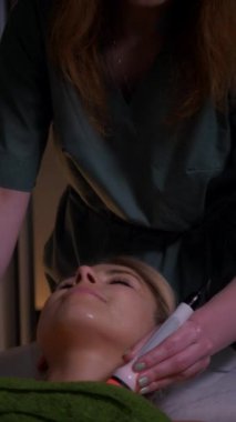 Dikey olarak, genç kadın spa salonunda profesyonel donanım titreşimli boyun masajı yaptırıyor. Güzel bir kız boynuna masaj yaptırıyor. Yakın plan çekim. Lüks profesyonel masaj anlayışı. Ağır çekimde çekmek.