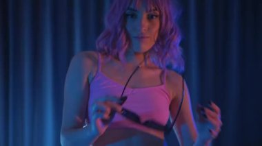 Siyah gözlüklü genç bir kadın erotik olarak ve pembe peruklu bir kadın kameraya bakıyor. Anime tarzı. Pembe iç çamaşırlı ve şortlu yarı traşlı kız karanlık alanda zarafetle hareket ediyor. yavaş çekim