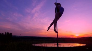 Mayo giymiş siluetli bir kadın güneşli bir alanda zarif bir şekilde dans ediyor. Alacakaranlık 'ta açık alanda dans eden zarif bir direk dansçısı. Meadow 'da bir direkte dans eden kadın için güzel bir günbatımı arkaplanı. Kuruluma karşı kadın direk dansı becerileri sergiliyor 