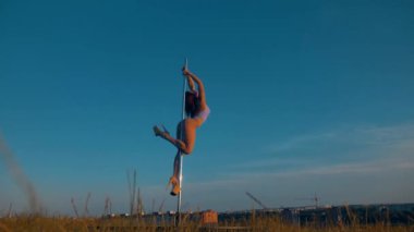 Kadın zarif bir şekilde gökyüzü zemininde dans ediyor. Polonyalı dansçı dışarıda güç ve esneklik gösteriyor. Açık gökyüzünün altında zarif bir direk dansı. Kadın dansçı, mavi bir arka plana karşı direkte hassas hareketler yapıyor.. 
