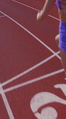 Dikey. Stadyumda koşan genç bir kadın. Pistte koşan bayan sporcu. Koşu pistinde koşan güzel bir bayan atlet. Şortlu kararlı bir kadın ve güneşli havalarda yolda..