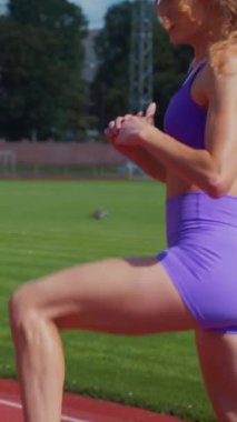 Dikey. Genç bir kadın antrenmana hazırlanıyor. Spor meraklısı koşu parkurunda topallıyor. Hareketli kadın egzersiz öncesi esneme hareketleri yapıyor.. 