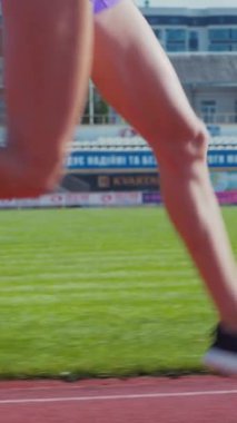 Dikey. Stadyumda koşan genç bir kadın. Pistte koşan bayan sporcu. Koşu pistinde koşan güzel bir bayan atlet. Şortlu kararlı bir kadın ve güneşli havalarda yolda..
