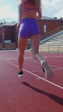 Dikey. Stadyumda koşan genç bir kadın. Pistte koşan bayan sporcu. Koşu pistinde koşan güzel bir bayan atlet. Şortlu kararlı bir kadın ve güneşli havalarda yolda..