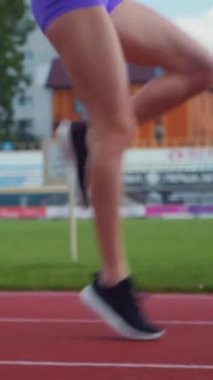 Dikey. Stadyumda koşan genç bir kadın. Pistte koşan bayan sporcu. Koşu pistinde koşan güzel bir bayan atlet. Şortlu kararlı bir kadın ve güneşli havalarda yolda..