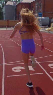 Dikey. Stadyumda koşan genç bir kadın. Pistte koşan bayan sporcu. Koşu pistinde koşan güzel bir bayan atlet. Şortlu kararlı bir kadın ve güneşli havalarda yolda..