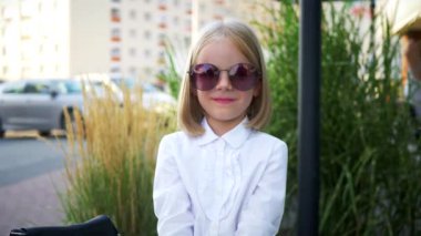 Beyaz gömlekli ve siyah pantolonlu genç bir kız kaldırımda duruyor, gülümsüyor ve kameraya bakıyor. Şehir kaldırımında kendine güvenen bir duruşu olan beyaz bluz ve siyah pantolon giyen küçük bir kız. Beyaz gömlek giyen neşeli bir kız 