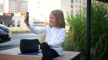 Güneş gözlüğü takan, cep telefonuyla konuşan, iş merkezinin yakınında kendinden emin ve neşeli görünen küçük bir kız. Video iletişimi, Skype. Telefonuyla selfie çeken, gülümseyen bir kız. İş kadını. Gülümseyen iş 