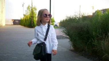 Beyaz gömlekli ve siyah pantolonlu genç bir kız sokaktaki bir iş merkezinin arka planında komik bir şekilde dans ediyor. Genç iş kadını mutlu. Şehir merkezinde kaldırımda yürürken kendi dünyasına dalmış şık bir çocuk..