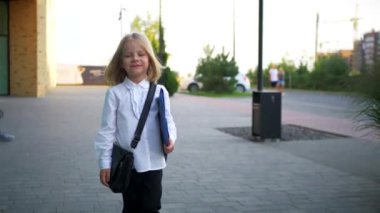 Beyaz gömlekli ve siyah pantolonlu genç bir kız kaldırımda duruyor, gülümsüyor ve kameraya bakıyor. Şehir kaldırımında kendine güvenen bir duruşu olan beyaz bluz ve siyah pantolon giyen küçük bir kız. Beyaz gömlek giyen neşeli bir kız 