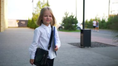 Beyaz gömlekli ve siyah pantolonlu genç bir kız kaldırımda duruyor, gülümsüyor ve kameraya bakıyor. Şehir kaldırımında kendine güvenen bir duruşu olan beyaz bluz ve siyah pantolon giyen küçük bir kız. Beyaz gömlek giyen neşeli bir kız 