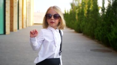 Beyaz gömlekli ve siyah pantolonlu genç bir kız sokaktaki bir iş merkezinin arka planında komik bir şekilde dans ediyor. Genç iş kadını mutlu. Şehir merkezinde kaldırımda yürürken kendi dünyasına dalmış şık bir çocuk..