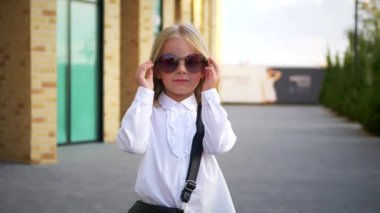 Beyaz gömlekli ve siyah pantolonlu genç bir kız kaldırımda duruyor, gülümsüyor ve kameraya bakıyor. Şehir kaldırımında kendine güvenen bir duruşu olan beyaz bluz ve siyah pantolon giyen küçük bir kız. Beyaz gömlek giyen neşeli bir kız 