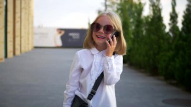 Güneş gözlüğü takan, cep telefonuyla konuşan, iş merkezinin yanında kendinden emin ve neşeli görünen küçük bir kız. Telefonla gülümseyen bir girişimci. Şık güneş gözlüklü genç bir kız, hareketli bir şekilde cep telefonuyla konuşuyor.