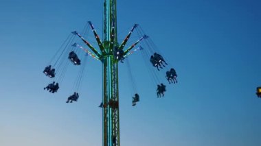 Gece gökyüzüne karşı parlayan ışıklarla süslenmiş canlı bir eğlence gezisi. Luna Parkı. Parlak yeşil ışıklar lunaparktaki dönen bir atlıkarıncanın üzerinde dans ediyor. Ekstrem atlıkarınca neşeyle döner, büyüleyici yeşil ışıklarla aydınlatılır. çekim gücü