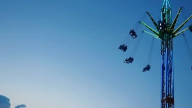 Gece gökyüzüne karşı parlayan ışıklarla süslenmiş canlı bir eğlence gezisi. Luna Parkı. Parlak yeşil ışıklar lunaparktaki dönen bir atlıkarıncanın üzerinde dans ediyor. Ekstrem atlıkarınca neşeyle döner, büyüleyici yeşil ışıklarla aydınlatılır. çekim gücü