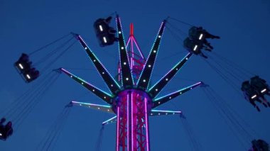 Gece gökyüzüne karşı parlayan ışıklarla süslenmiş canlı bir eğlence gezisi. Luna Parkı. Parlak yeşil ışıklar lunaparktaki dönen bir atlıkarıncanın üzerinde dans ediyor. Ekstrem atlıkarınca neşeyle döner, büyüleyici yeşil ışıklarla aydınlatılır. çekim gücü
