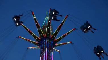 Gece gökyüzüne karşı parlayan ışıklarla süslenmiş canlı bir eğlence gezisi. Luna Parkı. Parlak yeşil ışıklar lunaparktaki dönen bir atlıkarıncanın üzerinde dans ediyor. Ekstrem atlıkarınca neşeyle döner, büyüleyici yeşil ışıklarla aydınlatılır. çekim gücü