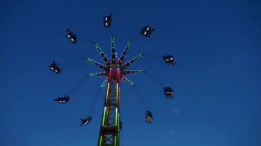 Gece gökyüzüne karşı parlayan ışıklarla süslenmiş canlı bir eğlence gezisi. Luna Parkı. Parlak yeşil ışıklar lunaparktaki dönen bir atlıkarıncanın üzerinde dans ediyor. Ekstrem atlıkarınca neşeyle döner, büyüleyici yeşil ışıklarla aydınlatılır. çekim gücü